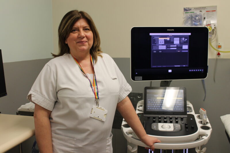 An ultrasound assistant stands next to an ultrasound machine