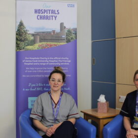 Two ladies sitting on chairs next to a banner and table